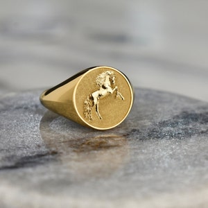 Puede incluir: Un anillo de sello de oro con un dise&ntilde;o en relieve de un caballo en la cara del anillo.