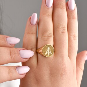Puede incluir: Un anillo de sello de oro con una cara circular que presenta un dise&ntilde;o de abeja grabado. El anillo tiene un acabado pulido y una banda lisa y redondeada que se estrecha hacia la parte posterior, mostrando un insecto detallado en el centro.