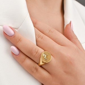 Puede incluir: Un anillo de sello de oro con un dise&ntilde;o en relieve de un caballo en la cara del anillo.