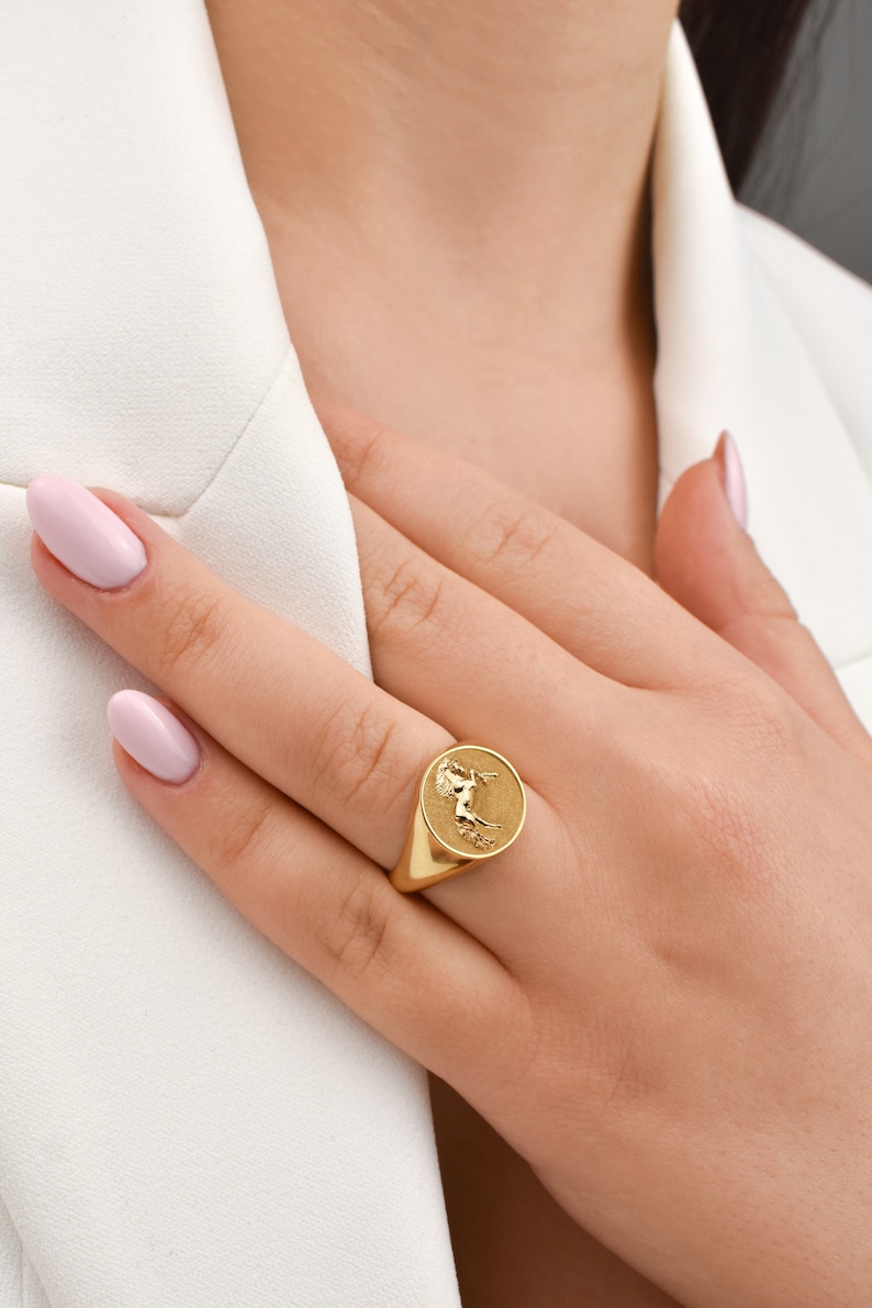 Puede incluir: Un anillo de sello de oro con un dise&ntilde;o en relieve de un caballo en la cara del anillo.