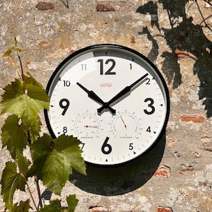 May include: A black and white outdoor clock with a thermometer and hygrometer. The clock face has black numbers and hands, and the words "CLOVONGLA FACTORY" are printed in red.