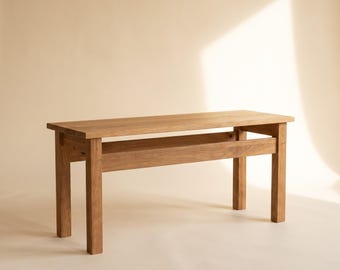 May include: A rectangular wooden bench featuring a natural light brown wood grain finish. The bench is constructed with four sturdy vertical legs and a horizontal support shelf positioned between the legs, beneath the flat rectangular seat.