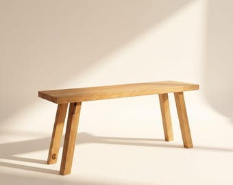 May include: A rectangular wooden bench featuring a smooth, light brown grain finish. The bench is supported by four sturdy, angled legs that extend outward from the seat, providing a stable base for this functional piece of furniture.