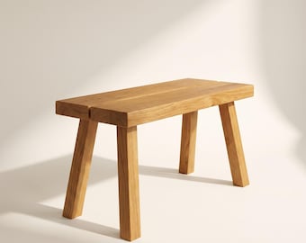 May include: A rectangular wooden bench constructed from light brown timber. The seat consists of two thick, parallel planks with a visible gap between them. It is supported by four sturdy, angled legs that extend outward from the corners.