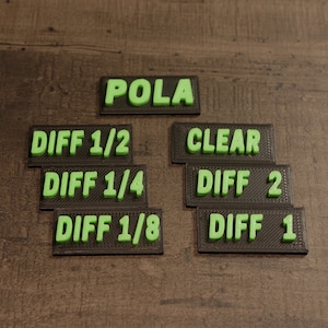 Peut inclure: Étiquettes en plastique noires et vertes avec les mots "POLA", "CLEAR", "DIFF 1/2", "DIFF 1/4", "DIFF 1/8", "DIFF 2" et "DIFF 1" imprimés dessus.