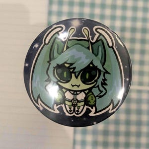Könnte beinhalten: Ein runder Button mit einem Cartoon-Alien-Design. Das Alien hat große grüne Augen, türkisfarbenes Haar und ein weißes Outfit. Der Hintergrund ist dunkelblau mit weißen Sternen, und der Rand ist weiß mit türkisfarbenen Konturen.