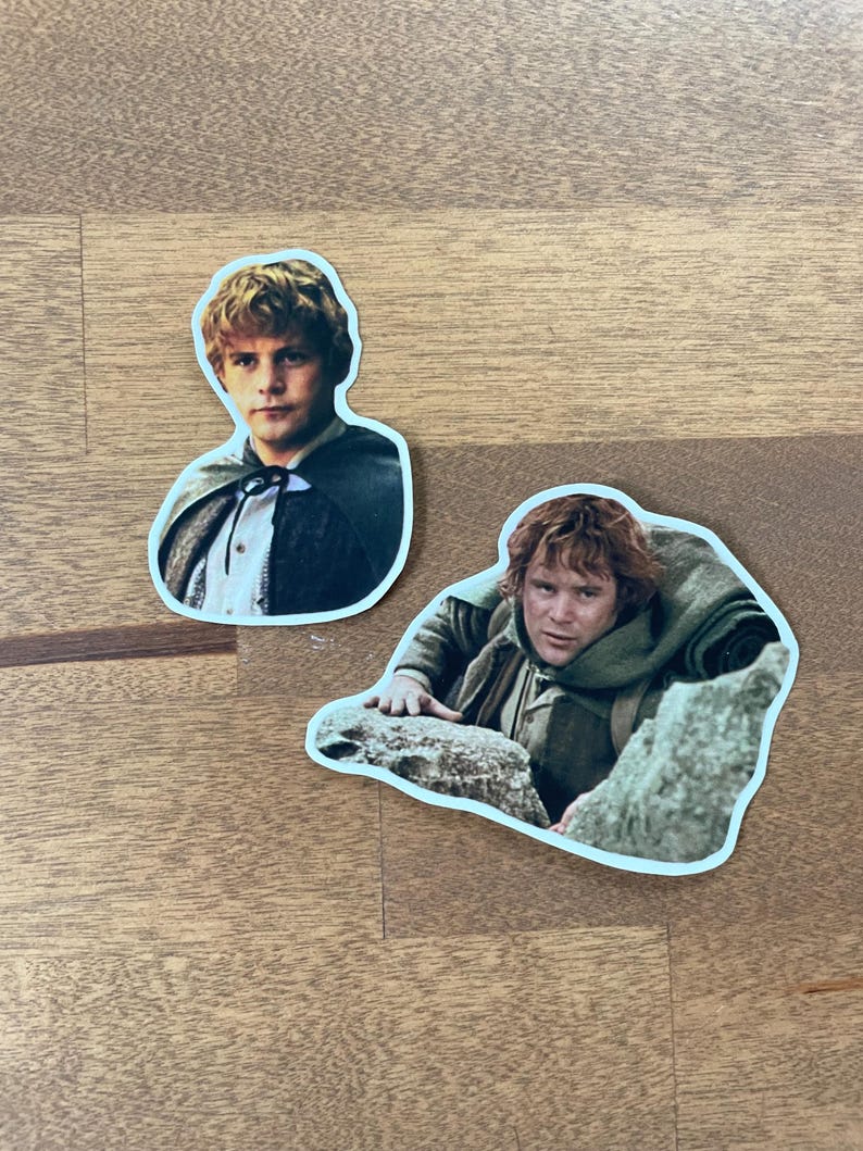 May include: Two stickers featuring characters from The Lord of the Rings. The first sticker shows a young man with brown hair and a brown cloak. The second sticker shows a man with brown hair and a brown beard, wearing a brown cloak and holding onto a rock.