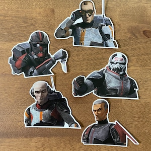 May include: Five Star Wars: The Bad Batch character stickers. The stickers feature the characters Hunter, Wrecker, Tech, Echo, and Crosshair. The stickers are printed on white paper and have a glossy finish.