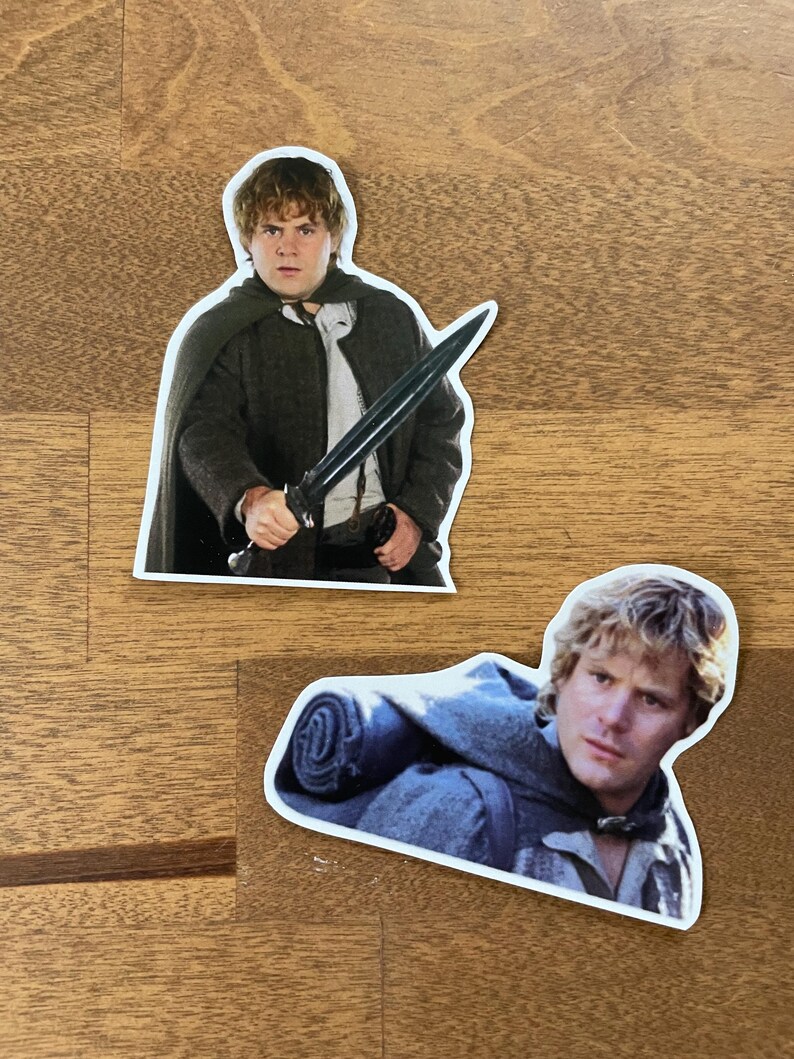 May include: Two stickers featuring characters from the Lord of the Rings movie franchise. The first sticker shows a character holding a sword, while the second sticker shows a character with a backpack.