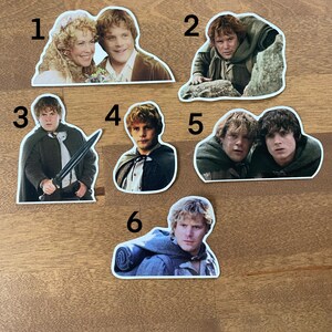 May include: Six different stickers featuring characters from the Lord of the Rings movie franchise. The stickers are printed on white paper and feature images of Frodo, Sam, Aragorn, and others.