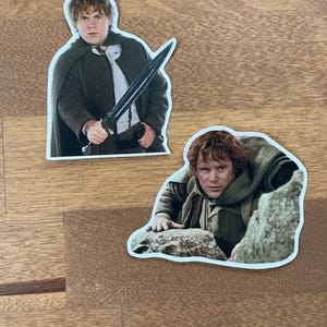 May include: Two stickers featuring images of a character from the Lord of the Rings movie. The first sticker shows the character holding a sword. The second sticker shows the character climbing a rock.