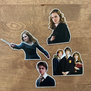 May include: Four Harry Potter character stickers. The stickers feature Hermione Granger, Harry Potter, Ron Weasley, and Ginny Weasley. The stickers are printed on white paper with a glossy finish.