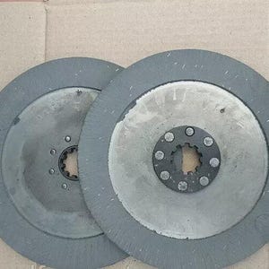May include: Two gray and silver circular clutch discs. Each disc has a central hub with bolt holes and a toothed inner ring. The outer edges are a darker gray, and the centers are a lighter silver color.