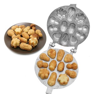 May include: A silver metal waffle iron with a handle. The iron has 12 molds in the shape of different woodland creatures, such as mushrooms, acorns, and leaves. The iron is open and shows a batch of freshly baked waffles in the molds.