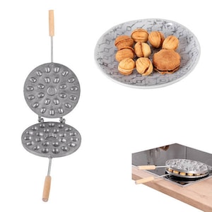 May include: A silver waffle iron with a wooden handle, open to reveal a round, non-stick surface with multiple indentations shaped like nuts. The waffle iron is used to make small, round cookies. A plate of cookies is shown in the background.