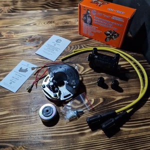 Puede incluir: Un kit de sistema de encendido para motocicleta con una bobina de encendido negra, un módulo de encendido plateado, dos cables de bujía negros y un arnés de cables amarillo. El kit también incluye una pequeña bolsa de hardware y dos manuales de instrucciones.