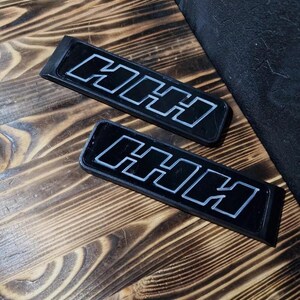 May include: Two black rectangular plaques with the word "HHH" in white raised lettering.