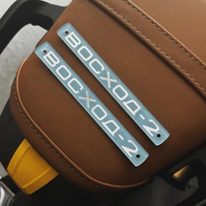 May include: Two light blue rectangular plates with the text "BOCXOД-2" in white lettering. The plates are placed on a brown leather surface. The plates have rounded corners and small holes.