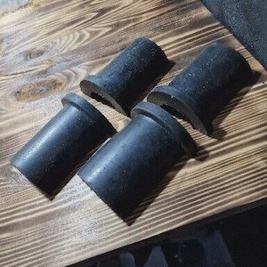 Op de afbeelding: Vier zwarte cilindrische rubberen objecten met een uitlopende basis liggen op een houten oppervlak. De objecten zijn gelijkmatig verdeeld en lijken componenten te zijn. De houtnerf is zichtbaar.
