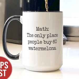 May include: White ceramic coffee mug with a black handle and rim. The mug has the text "Math: The only place people buy 60 watermelons." Coffee is being poured into the mug. A red circle with the words "SHIPS FAST" is in the lower left corner.