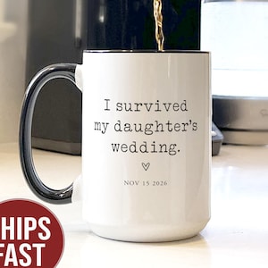 May include: White ceramic mug with a black handle and rim. The mug has the text "I survived my daughter's wedding." with a heart symbol and the date "NOV 15 2026." Coffee is being poured into the mug.