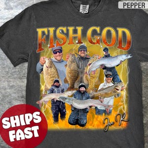 Pode incluir: Uma camiseta preta com uma estampa gr&aacute;fica de um grupo de homens segurando peixes. O gr&aacute;fico est&aacute; em um estilo retr&ocirc; com um fundo amarelo e laranja e raios. O texto "FISH GOD" est&aacute; impresso em letras grandes amarelas na parte superior do gr&aacute;fico. O texto "Joe R" est&aacute; impresso em branco na parte inferior do gr&aacute;fico.