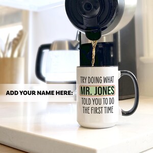 May include: A white coffee mug with a black handle and rim is being filled with coffee. The mug has the text "TRY DOING WHAT MR. JONES TOLD YOU TO DO THE FIRST TIME" in black and green. The words "ADD YOUR NAME HERE:" are also visible.