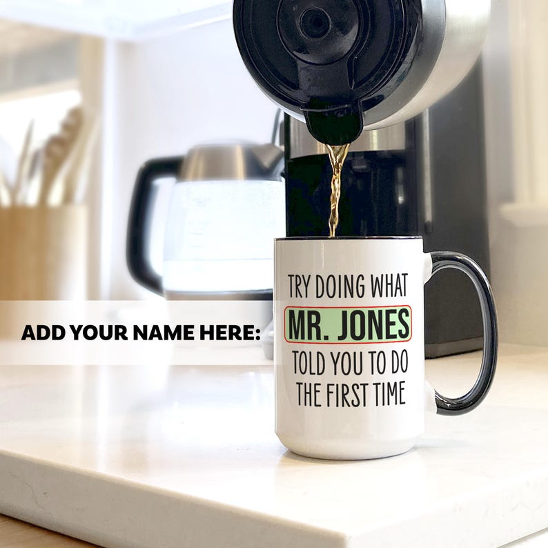 May include: A white coffee mug with a black handle and rim is being filled with coffee. The mug has the text "TRY DOING WHAT MR. JONES TOLD YOU TO DO THE FIRST TIME" in black and green. The words "ADD YOUR NAME HERE:" are also visible.