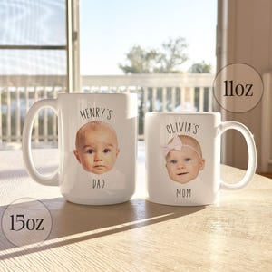 May include: Two white ceramic mugs, one 15oz and one 11oz, with baby photos and text. The larger mug says "Henry's Dad" and the smaller mug says "Olivia's Mom". The mugs are on a light-colored wooden surface.