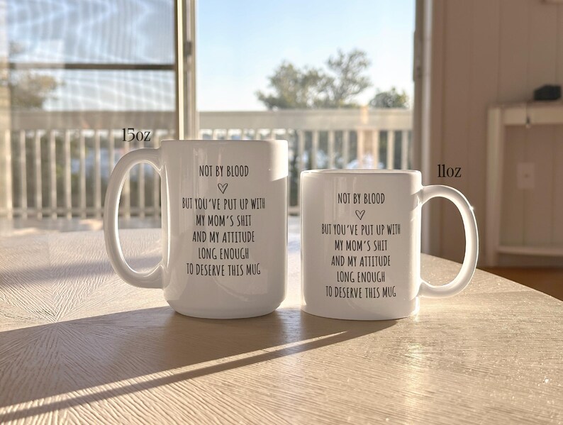 May include: Two white ceramic mugs, 15oz and 11oz, with a curved handle. The mugs have the same black text: "NOT BY BLOOD, BUT YOU'VE PUT UP WITH MY MOM'S SHIT AND MY ATTITUDE LONG ENOUGH TO DESERVE THIS MUG."