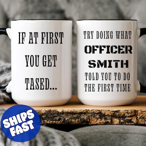 May include: Two white ceramic mugs with black rims and handles. The mug on the left has the text "If at first you get tased..." printed on it. The mug on the right has the text "Try doing what Officer Smith told you to do the first time" printed on it.