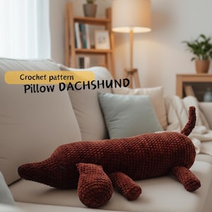 Könnte beinhalten: Ein gehäkeltes Dackel-Kissen in einem rötlich-braunen Farbton liegt auf einem cremefarbenen Sofa. Das Kissen hat einen langen Körper, kurze Beine und einen Schwanz. Der Text auf dem Bild lautet "Crochet pattern Pillow DACHSHUND".