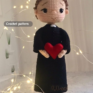 May include: A crocheted doll of a person in a black robe, holding a red heart. The doll has brown hair and a white collar. The text "Crochet pattern" is in the upper left corner.