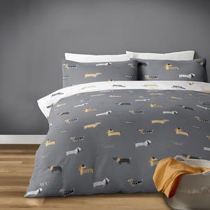 May include: Gray duvet cover and pillowcases set with a repeating pattern of dachshund dogs in various colors. The bedding set includes a duvet cover and two pillowcases. The duvet cover has a white underside. A basket with an orange blanket is in the corner.