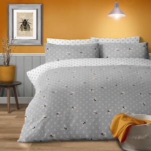 Può includere: Set di biancheria da letto grigio e bianco a tema api con motivo a nido d'ape. Il set include un copripiumino e federe, adornati con piccole illustrazioni di api. Una stampa di api incorniciata è appesa al muro, completando l'arredamento della camera da letto.