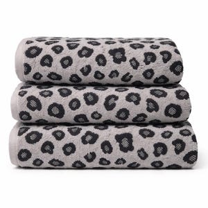 Puede incluir: Una pila de tres toallas de baño rectangulares con un color base gris claro y un patrón de leopardo negro repetitivo. Cada toalla tiene una superficie de tela suave y texturizada, doblada cuidadosamente para mostrar el diseño animal.