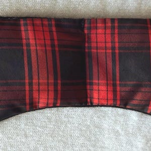 May include: A red and black plaid eye mask. The mask is rectangular with rounded edges and a curved bottom. The plaid pattern features thick red and black lines. The mask is designed to block out light.