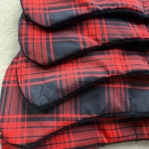 May include: Close-up of several red and black plaid fabric items. The fabric has a classic tartan pattern with a black border. The items appear to be layered, with the edges of each piece visible.