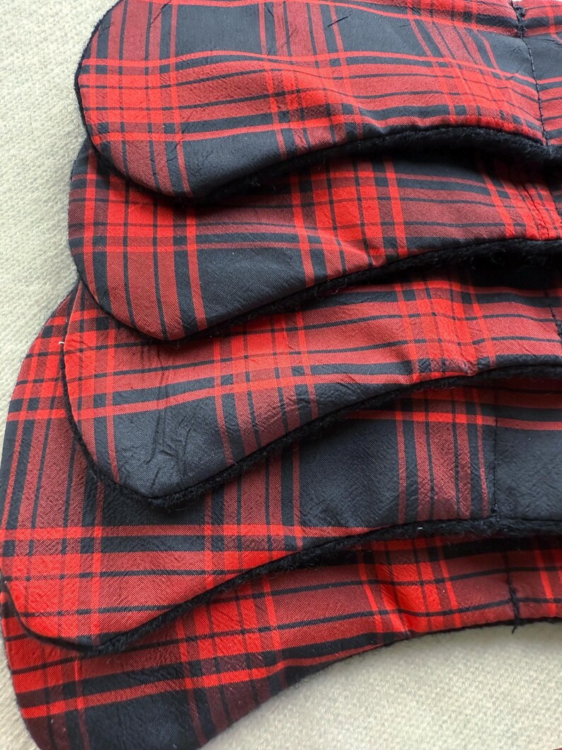 May include: Close-up of several red and black plaid fabric items. The fabric has a classic tartan pattern with a black border. The items appear to be layered, with the edges of each piece visible.