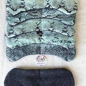 May include: Five eye masks with a teal and black snakeskin print are stacked together. A single dark grey eye mask is also present. A floral "handmade" sticker is visible.