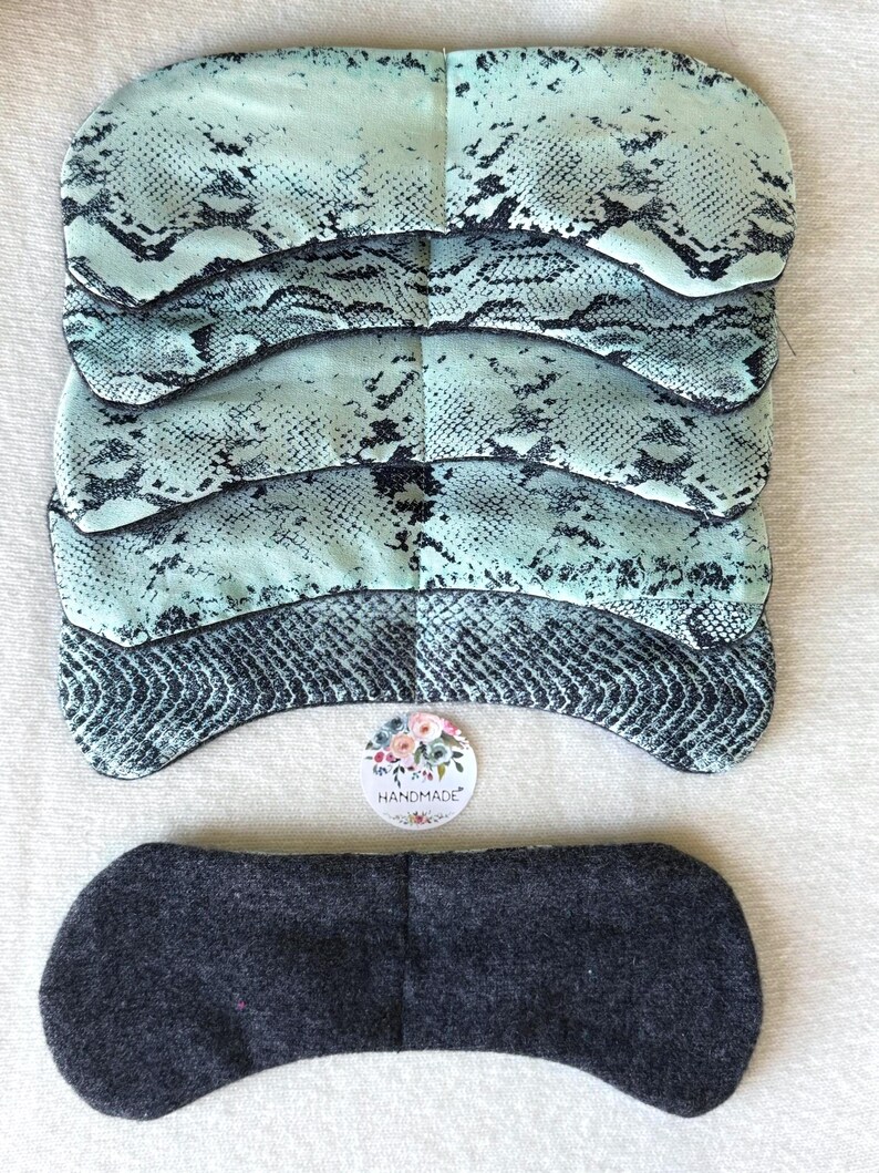 May include: Five eye masks with a teal and black snakeskin print are stacked together. A single dark grey eye mask is also present. A floral "handmade" sticker is visible.