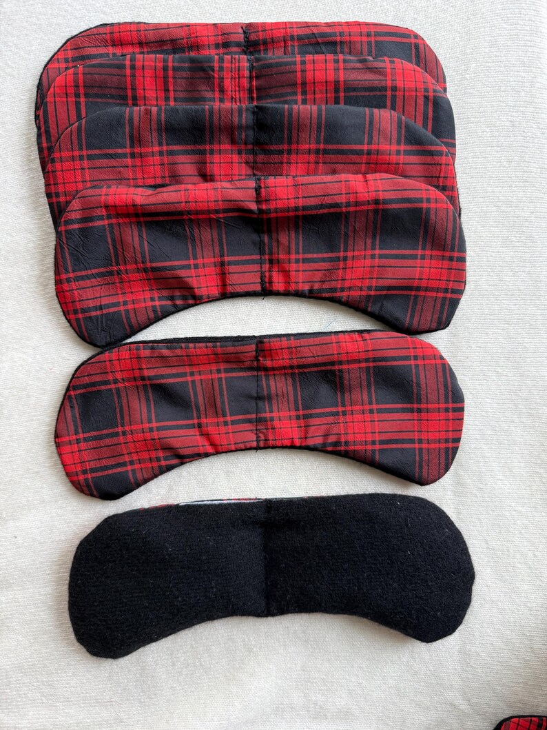 May include: Several eye masks in a plaid pattern of red and black are displayed. One mask is black. The masks are made of fabric and are designed to block out light. The masks are designed to be worn over the eyes.