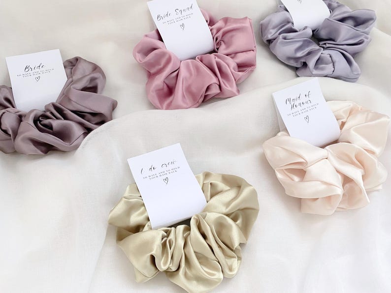May include: Set of five satin scrunchies with different colors and text cards. The cards have different titles, including "Bride", "Bride Squad", "Maid of Honour", and "I do Crew".