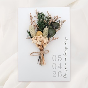 Puede incluir: Una tarjeta blanca con un ramo de flores secas atado con hilo. El ramo incluye flores verdes, beige y amarillas. La tarjeta tiene el texto "On your wedding day" y la fecha "05 04 26" en gris.