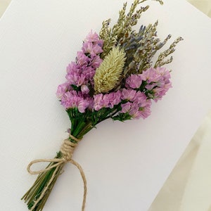 Op de afbeelding: Een klein boeket gedroogde bloemen gebonden met touw. Het boeket bevat roze bloemen, lavendel en gedroogd gras.