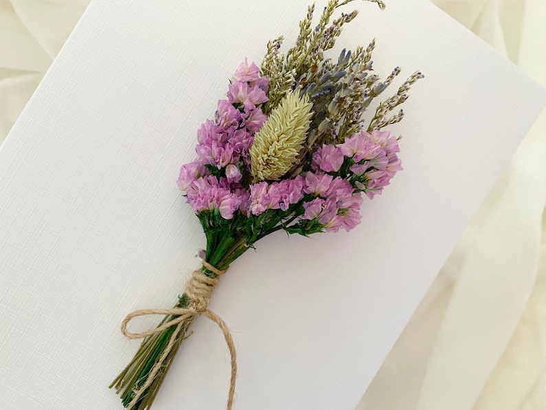 Op de afbeelding: Een klein boeket gedroogde bloemen gebonden met touw. Het boeket bevat roze bloemen, lavendel en gedroogd gras.