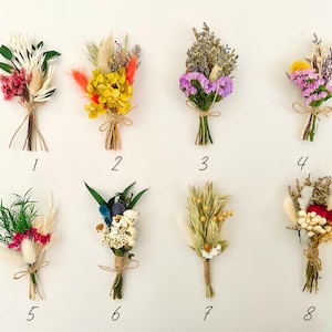 Op de afbeelding: Acht kleine boeketten gedroogde bloemen, elk gebonden met touw en genummerd van 1 tot en met 8. De boeketten bevatten een verscheidenheid aan kleuren en texturen, waaronder roze, paars, geel, wit en rood.