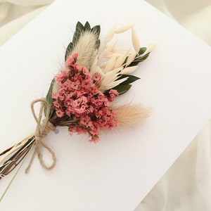 May include: A small bouquet of dried flowers tied with twine. The bouquet includes pink flowers, white dried grasses, and green leaves.