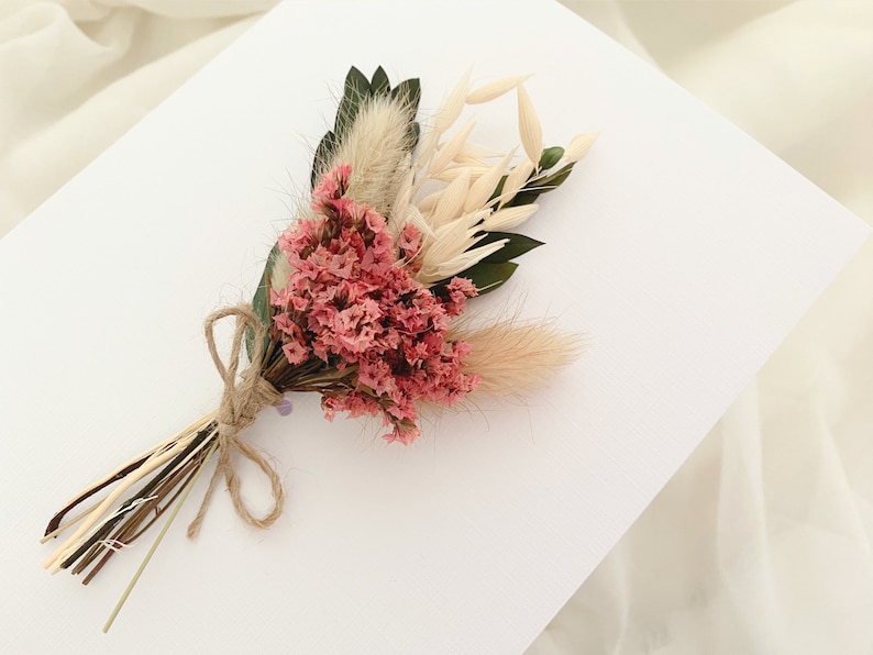 May include: A small bouquet of dried flowers tied with twine. The bouquet includes pink flowers, white dried grasses, and green leaves.