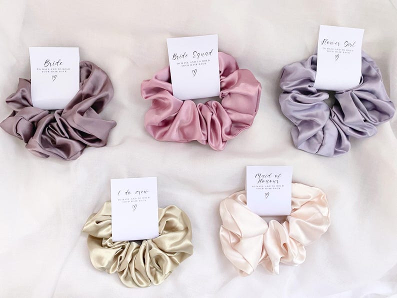 May include: Set of six satin scrunchies with different wedding party titles printed on cards. The scrunchies are in shades of pink, purple, beige, and cream.